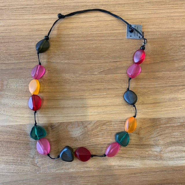 This zesty necklace features colorful translucent resin beads in bright colors such as pink, green, orange, and red. The handmade beads hang sporadically from a thin black wax cord. This adjustable necklace can be worn at your preferred length. Layer this necklace over a sold tee or dress and pair with coordinating earrings.  Adjustable Length:18